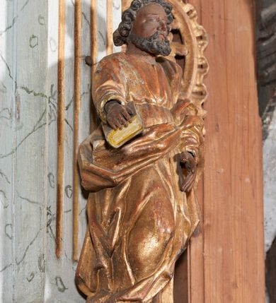 Zdjęcie nr 3: Figura nieopracowana z tyłu; ustawiona na niskiej, nieregularnej podstawie. Święty ukazany frontalnie, z prawą nogą ugiętą, obie ręce wyciąga wprzód, w prawej przytrzymuje księgę. Twarz ma pociągłą, o niewielkich, wąskich oczach, krótkim nosie i małych ustach, okoloną krótkimi, silnie kręconymi włosami i brodą. Ubrany jest w obficie fałdowaną tunikę przepasaną w talii oraz płaszcz zarzucony na lewe ramię i zawinięty z przodu postaci. Polichromia ciała naturalistyczna, szaty złocone. 