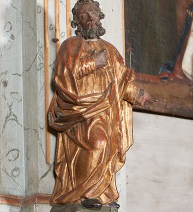 Zdjęcie nr 4: Figura nieopracowana z tyłu; ustawiona na niskiej, nieregularnej podstawie. Święty ukazany frontalnie z prawą nogą ugiętą, lewą rękę wyciąga w bok, prawą kładzie na piersi. Twarz ma pociągłą o niskim czole, niewielkich oczach, krótkim, wąskim nosie i małych ustach, okoloną krótkimi kręconymi włosami i brodą. Ubrany jest w obficie fałdowaną, tunikę przepasaną w talii oraz płaszcz zarzucony na ramiona i zawinięty z przodu postaci. Polichromia ciała naturalistyczna, szaty złocone.




