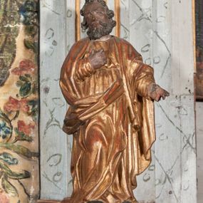 Zdjęcie nr 1: Figura nieopracowana z tyłu; ustawiona na niskiej, nieregularnej podstawie. Święty ukazany frontalnie z prawą nogą ugiętą, lewą rękę wyciąga w bok, prawą kładzie na piersi. Twarz ma pociągłą o niskim czole, niewielkich oczach, krótkim, wąskim nosie i małych ustach, okoloną krótkimi kręconymi włosami i brodą. Ubrany jest w obficie fałdowaną, tunikę przepasaną w talii oraz płaszcz zarzucony na ramiona i zawinięty z przodu postaci. Polichromia ciała naturalistyczna, szaty złocone.




