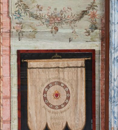 Zdjęcie nr 9: Ściany prezbiterium dekorowane malowanymi zielono-różowymi płycinami w formie stojących prostokątów, ujętymi iluzjonistycznymi ramkami, z malowaną dekoracją w formie kwiatowych festonów w górnej części oraz fantazyjnych dekoracji roślinno-kandelabrowych i wazonów z ornamentem roślinnym w dolnej. Płyciny umieszczone są między oknami ujętymi w malowane prostokątne opaski, pod którymi znajdują się zacheuszki. Na południowej ścianie znajdują się dwa okna, na północnej dwa pozorne okna, z których jedno przesłania ambona. Zacheuszki w formie malowanych migdałowatych medalionów z krzyżami w polach, na iluzjonistycznych wspornikach o klasycyzującej dekoracji, na tle niebieskich owalnych medalionów ujętych u góry wieńcem laurowym i u dołu dekoracją roślinną. Prezbiterium zamknięte trójbocznie, z podkreślonymi polichromią dwiema parami zwielokrotnionych pilastrów, flankujących ołtarz główny. Za ołtarzem, na każdej z trzech ścian analogicznie malowane płyciny. Dolny pas wszystkich ścian prezbiterium opasuje malowany iluzjonistycznie jasnobrązowy i marmoryzowany cokół, dekorowany płycinami w formie leżącego prostokąta i zamknięty profilowaniem. Ściany prezbiterium zamknięte od góry drewnianym gzymsem pokrytym malowanymi iluzjonistycznie elementami profili z kostkowaniem i jajownikiem.
Sklepienie w części prezbiterialnej w formie malowanego nieba, wypełnionego obłokami. Nad gzymsem malowana iluzjonistycznie kamienna balustrada z ośmioma wazonami na cokołach umieszczonych na osiach wydzielających podziały ścian prezbiterium, z motywem stylizowanego biegnącego psa stanowiącym wypełnienie balustrady. Pomiędzy wazonami ukazani jako stojący za balustradą i widoczni w półpostaci aniołowie. Na północnej ścianie anioł trzymający w dłoniach zamknięta koronę, z napisem „PRINCIPATUS” oraz anioł ubrany w zbroję i hełm z białą chorągwią w prawej ręce, podpisany „ARCHANGELI”. Na południowej ścianie anioł ubrany w suknię i płaszcz, który prawą ręką wskazuje niebo, lewą zaś tuli do siebie dziecko, podpisany „ANGELI” oraz anioł ubrany w suknię i płaszcz, który lewą rękę kładzie na piersi, w prawej trzyma miecz skierowany ostrzem w dół, podpisany „DOMINATIONES”. W centralnej części sklepienia ujęta obłokami z malowanym u dołu aniołem scena ekstazy św. Marii Magdaleny. Ukazuje ona omdlewającą na skałach świętą, której towarzyszą aniołowie. Maria Magdalena przedstawiona z profilu, jako siedząca, odchylona w tył, z opadającą głową i rękami. Ubrana w biało-niebieską suknię odsłaniającą ramiona. Włosy ma długie, opadające na plecy i pierś. Nad głową nimb. Za nią i obok niej siedzą dwaj aniołowie, który podtrzymują jej opadające ciało. Przy prawym boku świętej znajduje się krucyfiks, natomiast w dolnej części sceny, na ziemi leżą: czaszka, dyscyplina, otwarta księga i puszka na wonności. W górnej części sceny ukazane rozświetlone niebo, z którego wyłania się wiązka światła, a wokół ukazane są trzy uskrzydlone główki anielskie. Na ścianie zachodniej prezbiterium, nad łukiem tęczowym napis: „Roku Pańskiego 1565 kościół ten zbudowany przez wielmożnego Pana Spytka Jordana, poświęcony przez najjaśniejszego i przewielebnego Pana Tomasza Oborskiego, Biskupa Loadycejskiego, Syfragana Krakowskiego w Roku Pańskim 1634 w dniu 5 czerwca. Odnowiony całkowicie i ozdobiony ołtarzami wraz z organami i chórem przez plebana w Roku pańskim 1778. Odmalowany zaś kosztem tegoż plebana w Roku Pańskim 1802. A[ndrzej] A[ntałkiewicz]”. Za ołtarzem głównym drugi napis: „Restau/rata Hoc / Ecclesia / AD 1777 / Finita 23 / Septembris”.
W korpusie nawowym polichromia o analogicznej formie. Na ścianach północnej i południowej malowane płyciny pomiędzy oknami, okna w malowanych opaskach z zacheuszkami w formie medalionów poniżej. Ściana tęczowa zdobiona malowanymi płycinami, łuk ujęty malowanym en grisaille owocowo-kwiatowym festonem, opadającym na wsporniki z malowanymi iluzjonistycznie elementami architektonicznymi. Ściana zachodnia w dolnej partii malowana analogicznie do ścian bocznych. Natomiast w górnej partii, od poziomu parapetu chóru muzycznego malowana iluzjonistycznie architektura w postaci opilastrowanego muru kamiennego i arkady pośrodku z apsydą o podziałach pilastrowych z malowanymi oknami, na której tle umieszczony jest organ. Zaskrzynienia z malowanymi prostokątnymi płycinami. Filary podtrzymujące zaskrzynienia malowane na sposób imitujący marmoryzację. Podpory podtrzymujące drewniany profilowany gzyms pokryty malowanymi iluzjonistycznie elementami profili z kostkowaniem i jajownikiem. Powyżej sklepienie z malowaną iluzjonistycznie balustradą, z trzech stron (północnej, wschodniej i południowej), analogiczną jak w prezbiterium, z wazonami na cokołach umieszczonymi na osiach podpór i z postaciami. Na ścianie północnej anioł trzymający w dłoniach koronę cierniową z podpisem „VIRTUTES”, anioł trzymający księgę i berło, z podpisem „SERAFIN” oraz anioł trzymający berło, bez podpisu. Na ścianie południowej anioł trzymający buławę, z napisem „POTESTATES”, anioł trzymający miecz skierowany w górę, z napisem „CHERUBIN” i wizerunek św. Franciszka serafickiego podczas stygmatyzacji. Na sklepieniu nawy przedstawione niebo wypełnione obłokami, pośrodku scena Koronacji Najświętszej Marii Panny, zamknięta owalem i otoczona obłokami. Scena ukazuje Chrystusa i Boga Ojca tronujących pośród obłoków z gołębicą Ducha Świętego w glorii promienistej unoszącą się nad nimi. Obaj trzymają koronę nad głową klęczącej poniżej Marii, której nogi spoczywają na globie i sierpie księżyca, a która stopami depcze węża. Grupa otoczona uskrzydlonymi główkami anielskimi, dwoma puttami i aniołem trzymającym w dłoni lilię. 
