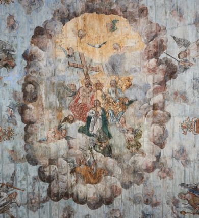 Zdjęcie nr 15: Ściany prezbiterium dekorowane malowanymi zielono-różowymi płycinami w formie stojących prostokątów, ujętymi iluzjonistycznymi ramkami, z malowaną dekoracją w formie kwiatowych festonów w górnej części oraz fantazyjnych dekoracji roślinno-kandelabrowych i wazonów z ornamentem roślinnym w dolnej. Płyciny umieszczone są między oknami ujętymi w malowane prostokątne opaski, pod którymi znajdują się zacheuszki. Na południowej ścianie znajdują się dwa okna, na północnej dwa pozorne okna, z których jedno przesłania ambona. Zacheuszki w formie malowanych migdałowatych medalionów z krzyżami w polach, na iluzjonistycznych wspornikach o klasycyzującej dekoracji, na tle niebieskich owalnych medalionów ujętych u góry wieńcem laurowym i u dołu dekoracją roślinną. Prezbiterium zamknięte trójbocznie, z podkreślonymi polichromią dwiema parami zwielokrotnionych pilastrów, flankujących ołtarz główny. Za ołtarzem, na każdej z trzech ścian analogicznie malowane płyciny. Dolny pas wszystkich ścian prezbiterium opasuje malowany iluzjonistycznie jasnobrązowy i marmoryzowany cokół, dekorowany płycinami w formie leżącego prostokąta i zamknięty profilowaniem. Ściany prezbiterium zamknięte od góry drewnianym gzymsem pokrytym malowanymi iluzjonistycznie elementami profili z kostkowaniem i jajownikiem.
Sklepienie w części prezbiterialnej w formie malowanego nieba, wypełnionego obłokami. Nad gzymsem malowana iluzjonistycznie kamienna balustrada z ośmioma wazonami na cokołach umieszczonych na osiach wydzielających podziały ścian prezbiterium, z motywem stylizowanego biegnącego psa stanowiącym wypełnienie balustrady. Pomiędzy wazonami ukazani jako stojący za balustradą i widoczni w półpostaci aniołowie. Na północnej ścianie anioł trzymający w dłoniach zamknięta koronę, z napisem „PRINCIPATUS” oraz anioł ubrany w zbroję i hełm z białą chorągwią w prawej ręce, podpisany „ARCHANGELI”. Na południowej ścianie anioł ubrany w suknię i płaszcz, który prawą ręką wskazuje niebo, lewą zaś tuli do siebie dziecko, podpisany „ANGELI” oraz anioł ubrany w suknię i płaszcz, który lewą rękę kładzie na piersi, w prawej trzyma miecz skierowany ostrzem w dół, podpisany „DOMINATIONES”. W centralnej części sklepienia ujęta obłokami z malowanym u dołu aniołem scena ekstazy św. Marii Magdaleny. Ukazuje ona omdlewającą na skałach świętą, której towarzyszą aniołowie. Maria Magdalena przedstawiona z profilu, jako siedząca, odchylona w tył, z opadającą głową i rękami. Ubrana w biało-niebieską suknię odsłaniającą ramiona. Włosy ma długie, opadające na plecy i pierś. Nad głową nimb. Za nią i obok niej siedzą dwaj aniołowie, który podtrzymują jej opadające ciało. Przy prawym boku świętej znajduje się krucyfiks, natomiast w dolnej części sceny, na ziemi leżą: czaszka, dyscyplina, otwarta księga i puszka na wonności. W górnej części sceny ukazane rozświetlone niebo, z którego wyłania się wiązka światła, a wokół ukazane są trzy uskrzydlone główki anielskie. Na ścianie zachodniej prezbiterium, nad łukiem tęczowym napis: „Roku Pańskiego 1565 kościół ten zbudowany przez wielmożnego Pana Spytka Jordana, poświęcony przez najjaśniejszego i przewielebnego Pana Tomasza Oborskiego, Biskupa Loadycejskiego, Syfragana Krakowskiego w Roku Pańskim 1634 w dniu 5 czerwca. Odnowiony całkowicie i ozdobiony ołtarzami wraz z organami i chórem przez plebana w Roku pańskim 1778. Odmalowany zaś kosztem tegoż plebana w Roku Pańskim 1802. A[ndrzej] A[ntałkiewicz]”. Za ołtarzem głównym drugi napis: „Restau/rata Hoc / Ecclesia / AD 1777 / Finita 23 / Septembris”.
W korpusie nawowym polichromia o analogicznej formie. Na ścianach północnej i południowej malowane płyciny pomiędzy oknami, okna w malowanych opaskach z zacheuszkami w formie medalionów poniżej. Ściana tęczowa zdobiona malowanymi płycinami, łuk ujęty malowanym en grisaille owocowo-kwiatowym festonem, opadającym na wsporniki z malowanymi iluzjonistycznie elementami architektonicznymi. Ściana zachodnia w dolnej partii malowana analogicznie do ścian bocznych. Natomiast w górnej partii, od poziomu parapetu chóru muzycznego malowana iluzjonistycznie architektura w postaci opilastrowanego muru kamiennego i arkady pośrodku z apsydą o podziałach pilastrowych z malowanymi oknami, na której tle umieszczony jest organ. Zaskrzynienia z malowanymi prostokątnymi płycinami. Filary podtrzymujące zaskrzynienia malowane na sposób imitujący marmoryzację. Podpory podtrzymujące drewniany profilowany gzyms pokryty malowanymi iluzjonistycznie elementami profili z kostkowaniem i jajownikiem. Powyżej sklepienie z malowaną iluzjonistycznie balustradą, z trzech stron (północnej, wschodniej i południowej), analogiczną jak w prezbiterium, z wazonami na cokołach umieszczonymi na osiach podpór i z postaciami. Na ścianie północnej anioł trzymający w dłoniach koronę cierniową z podpisem „VIRTUTES”, anioł trzymający księgę i berło, z podpisem „SERAFIN” oraz anioł trzymający berło, bez podpisu. Na ścianie południowej anioł trzymający buławę, z napisem „POTESTATES”, anioł trzymający miecz skierowany w górę, z napisem „CHERUBIN” i wizerunek św. Franciszka serafickiego podczas stygmatyzacji. Na sklepieniu nawy przedstawione niebo wypełnione obłokami, pośrodku scena Koronacji Najświętszej Marii Panny, zamknięta owalem i otoczona obłokami. Scena ukazuje Chrystusa i Boga Ojca tronujących pośród obłoków z gołębicą Ducha Świętego w glorii promienistej unoszącą się nad nimi. Obaj trzymają koronę nad głową klęczącej poniżej Marii, której nogi spoczywają na globie i sierpie księżyca, a która stopami depcze węża. Grupa otoczona uskrzydlonymi główkami anielskimi, dwoma puttami i aniołem trzymającym w dłoni lilię. 
