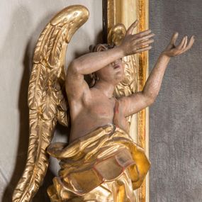 Zdjęcie nr 1: Figura ścięta i drążona z tyłu, ustawiona na niskiej podstawie. Anioł ukazany frontalnie, w kontrapoście, o esowato wygiętej sylwetce, obie ręce unosi wysoko, kierując je w lewą stronę. Twarz ma okrągłą, o pełnych policzkach i wyodrębnionej brodzie, migdałowatych oczach, prostym nosie i rozchylonych ustach, okoloną krótkimi, kręconymi, brązowymi włosami. Anioł ubrany w ekspresyjnie fałdowany, złocony płaszcz, podtrzymywany pojedynczą taśmą przełożoną przez lewe ramię, zawinięty wokół bioder, odsłaniający lewą nogę. Skrzydła ma duże, złożone i złocone. Przy prawej nodze postaci srebrzony obłok. Polichromia ciała naturalistyczna.  



