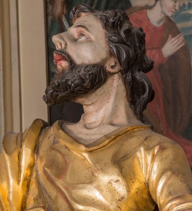 Zdjęcie nr 7: Figura ścięta z tyłu, drążona. Święty ukazany frontalnie, z uniesioną głową skierowaną w prawo, w kontrapoście, o esowato wygiętej sylwetce, odchylonej lekko w tył. W prawej ręce trzyma miecz, zwrócony ostrzem w dół, lewą przytrzymuje na nodze księgę. Twarz ma pociągłą, o dużych, migdałowatych oczach, zadartym nosie i pełnych ustach z wysuniętą górną wargą. Twarz okolona krótką, rozwidloną brodą oraz falowanymi włosami opadającymi na kark. Święty ubrany jest w sięgającą stóp tunikę z długimi rękawami, przepasaną szarfą oraz płaszcz zwinięty wokół prawego ramienia i opadający na lewą nogę. Polichromia ciała naturalistyczna, szaty i atrybuty złocone, detal srebrzony.