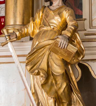 Zdjęcie nr 3: Figura ścięta z tyłu, drążona. Święty ukazany frontalnie, z uniesioną głową skierowaną w prawo, w kontrapoście, o esowato wygiętej sylwetce, odchylonej lekko w tył. W prawej ręce trzyma miecz, zwrócony ostrzem w dół, lewą przytrzymuje na nodze księgę. Twarz ma pociągłą, o dużych, migdałowatych oczach, zadartym nosie i pełnych ustach z wysuniętą górną wargą. Twarz okolona krótką, rozwidloną brodą oraz falowanymi włosami opadającymi na kark. Święty ubrany jest w sięgającą stóp tunikę z długimi rękawami, przepasaną szarfą oraz płaszcz zwinięty wokół prawego ramienia i opadający na lewą nogę. Polichromia ciała naturalistyczna, szaty i atrybuty złocone, detal srebrzony.