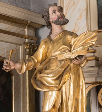 Zdjęcie nr 1: Figura ścięta z tyłu, drążona, ustawiona na niskiej podstawie. Święty ukazany frontalnie, z głową skierowaną w lewo, stoi w kontrapoście. Lewą ręką podtrzymuje otwartą księgę, prawą wyciąga w bok, a w dłoni trzyma klucz. Twarz ma pociągłą, o starczych rysach, migdałowatych oczach skierowanych w górę, lekko garbatym nosie oraz otwartych ustach z widoczną linią zębów. Okolona jest brodą, silnie wysuniętą do przodu oraz krótkimi, kręconymi włosami. Ubrany jest w tunikę z kołnierzykiem, przepasaną w talii, ściśle przylegającą do ciała w partii torsu oraz płaszcz przepasany diagonalnie przez lewe ramię i otaczający postać z wywiniętą połą na prawym boku. Polichromia ciała naturalistyczna, włosy ciemnobrązowe, szaty i atrybuty złocone. 

