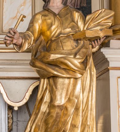 Zdjęcie nr 2: Figura ścięta z tyłu, drążona, ustawiona na niskiej podstawie. Święty ukazany frontalnie, z głową skierowaną w lewo, stoi w kontrapoście. Lewą ręką podtrzymuje otwartą księgę, prawą wyciąga w bok, a w dłoni trzyma klucz. Twarz ma pociągłą, o starczych rysach, migdałowatych oczach skierowanych w górę, lekko garbatym nosie oraz otwartych ustach z widoczną linią zębów. Okolona jest brodą, silnie wysuniętą do przodu oraz krótkimi, kręconymi włosami. Ubrany jest w tunikę z kołnierzykiem, przepasaną w talii, ściśle przylegającą do ciała w partii torsu oraz płaszcz przepasany diagonalnie przez lewe ramię i otaczający postać z wywiniętą połą na prawym boku. Polichromia ciała naturalistyczna, włosy ciemnobrązowe, szaty i atrybuty złocone. 

