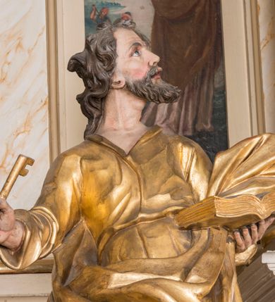 Zdjęcie nr 6: Figura ścięta z tyłu, drążona, ustawiona na niskiej podstawie. Święty ukazany frontalnie, z głową skierowaną w lewo, stoi w kontrapoście. Lewą ręką podtrzymuje otwartą księgę, prawą wyciąga w bok, a w dłoni trzyma klucz. Twarz ma pociągłą, o starczych rysach, migdałowatych oczach skierowanych w górę, lekko garbatym nosie oraz otwartych ustach z widoczną linią zębów. Okolona jest brodą, silnie wysuniętą do przodu oraz krótkimi, kręconymi włosami. Ubrany jest w tunikę z kołnierzykiem, przepasaną w talii, ściśle przylegającą do ciała w partii torsu oraz płaszcz przepasany diagonalnie przez lewe ramię i otaczający postać z wywiniętą połą na prawym boku. Polichromia ciała naturalistyczna, włosy ciemnobrązowe, szaty i atrybuty złocone. 

