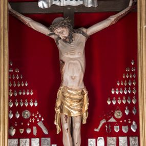 Zdjęcie nr 1: Figura Chrystusa żywego, ścięta z tyłu, przybita do krzyża trzema gwoździami. Ciało w lekkim zwisie, o ramionach układających się na kształt łuku, głowa opadająca na prawy bark, nogi wyprostowane, stopy skrzyżowane w układzie prawa na lewą. Chrystus ma pociągłą twarz, o wystających kościach policzkowych, dużych, półprzymkniętych oczach, długim, prostym nosie oraz szerokich, otwartych ustach z widoczną linią zębów. Twarz okolona jest krótką brodą silnie skręconą w pojedyncze pukle oraz falowanymi włosami opadającymi pojedynczymi pasmami na ramiona. Na głowie ma koronę cierniową. Jego ciało jest smukłe i wychudzone z podkreślonymi żebrami i mostkiem klatki piersiowej oraz ścięgnami w partii ramion i nóg. Stopy i dłonie ma nieproporcjonalnie duże. Prawy bok ma przebity, z widocznym dużym otworem oraz rzeźbioną, obficie broczącą krwią ze wszystkich ran. Perizonium sięgające połowy ud, silnie fałdowane, z dwoma kaskadowymi zwisami tkaniny na obu bokach. Ciało polichromowane naturalistycznie, o bladej karnacji, włosy i broda ciemnobrązowe, perizonium złocone. Na zakończeniu pionowej belki krzyża pozioma, srebrzona banderola z napisem „INRI”. 

