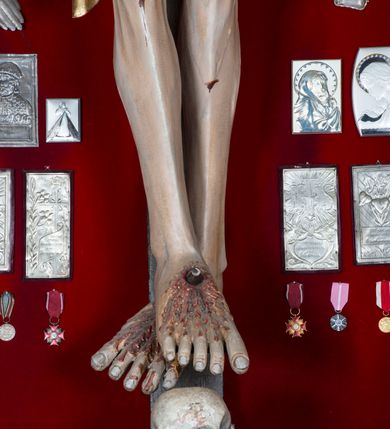 Zdjęcie nr 4: Figura Chrystusa żywego, ścięta z tyłu, przybita do krzyża trzema gwoździami. Ciało w lekkim zwisie, o ramionach układających się na kształt łuku, głowa opadająca na prawy bark, nogi wyprostowane, stopy skrzyżowane w układzie prawa na lewą. Chrystus ma pociągłą twarz, o wystających kościach policzkowych, dużych, półprzymkniętych oczach, długim, prostym nosie oraz szerokich, otwartych ustach z widoczną linią zębów. Twarz okolona jest krótką brodą silnie skręconą w pojedyncze pukle oraz falowanymi włosami opadającymi pojedynczymi pasmami na ramiona. Na głowie ma koronę cierniową. Jego ciało jest smukłe i wychudzone z podkreślonymi żebrami i mostkiem klatki piersiowej oraz ścięgnami w partii ramion i nóg. Stopy i dłonie ma nieproporcjonalnie duże. Prawy bok ma przebity, z widocznym dużym otworem oraz rzeźbioną, obficie broczącą krwią ze wszystkich ran. Perizonium sięgające połowy ud, silnie fałdowane, z dwoma kaskadowymi zwisami tkaniny na obu bokach. Ciało polichromowane naturalistycznie, o bladej karnacji, włosy i broda ciemnobrązowe, perizonium złocone. Na zakończeniu pionowej belki krzyża pozioma, srebrzona banderola z napisem „INRI”. 

