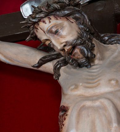 Zdjęcie nr 5: Figura Chrystusa żywego, ścięta z tyłu, przybita do krzyża trzema gwoździami. Ciało w lekkim zwisie, o ramionach układających się na kształt łuku, głowa opadająca na prawy bark, nogi wyprostowane, stopy skrzyżowane w układzie prawa na lewą. Chrystus ma pociągłą twarz, o wystających kościach policzkowych, dużych, półprzymkniętych oczach, długim, prostym nosie oraz szerokich, otwartych ustach z widoczną linią zębów. Twarz okolona jest krótką brodą silnie skręconą w pojedyncze pukle oraz falowanymi włosami opadającymi pojedynczymi pasmami na ramiona. Na głowie ma koronę cierniową. Jego ciało jest smukłe i wychudzone z podkreślonymi żebrami i mostkiem klatki piersiowej oraz ścięgnami w partii ramion i nóg. Stopy i dłonie ma nieproporcjonalnie duże. Prawy bok ma przebity, z widocznym dużym otworem oraz rzeźbioną, obficie broczącą krwią ze wszystkich ran. Perizonium sięgające połowy ud, silnie fałdowane, z dwoma kaskadowymi zwisami tkaniny na obu bokach. Ciało polichromowane naturalistycznie, o bladej karnacji, włosy i broda ciemnobrązowe, perizonium złocone. Na zakończeniu pionowej belki krzyża pozioma, srebrzona banderola z napisem „INRI”. 

