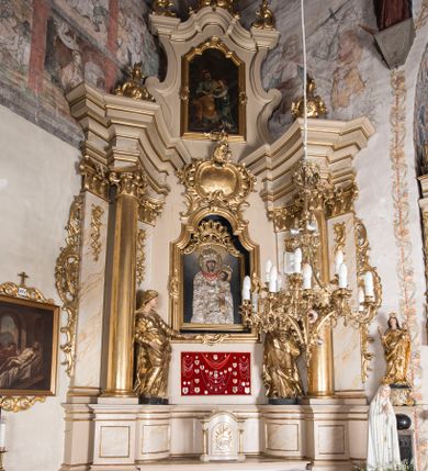Zdjęcie nr 1: Nastawa ołtarzowa architektoniczna, jednoosiowa, jednokondygnacyjna ze zwieńczeniem, ustawiona na dwustrefowym cokole z wyodrębnionymi prostopadłościanami. Ołtarz kamienny, prostopadłościenny, w drewnianej obudowie. Mensa kamienna z marmurowym portatylem. Antepedium drewniane, w kształcie leżącego prostokąta, ujęte profilowaną ramą, z płaskorzeźbionym monogramem maryjnym oraz fragmentami ornamentu roślinnego. Tabernakulum w kształcie prostopadłościennej skrzynki o wypukłym licu, flankowanej parą kolumienek na cokołach, ustawionych pod kątem, dźwigających woluty oraz gzyms przyjmujący formę łuku segmentowego nadwieszonego. Drzwiczki w kształcie stojącego prostokąta zamkniętego łukiem półkolistym, w opasce, z płaskorzeźbionym przedstawieniem baranka apokaliptycznego, leżącego na księdze, w glorii. Nastawa ujęta dwiema parami pilastrów dekorowanych rocaille&#039;em i stojącą pomiędzy nimi parą kolumn o kapitelach kompozytowych dźwigających pełne belkowanie, wyłamane na ich osi, przerwane pośrodku. Na belkowaniu ustawione dwa wazony. W polu centralnym głęboka wnęka w formie stojącego prostokąta zamkniętego łukiem półkolistym nadwieszonym z uskokiem, ujęta profilowaną ramą, z obrazem Matki Boskiej z Dzieciątkiem w osobnej profilowanej ramie o kształcie stojącego prostokąta zamkniętego ornamentalnym łukiem. Ponad nią, w partii belkowania rokokowy kartusz z rytym monogramem Marii, a poniżej prostokątna płycina z wotami. Pole flankowane dwiema figurami kobiet stojącymi na ćwierćkolistych cokołach. Nastawa ujęta uszami utworzonymi z rocaille&#039;u. Zwieńczenie w formie stojącego prostokąta o wklęsłych bokach, ze spływami z uszakami po bokach, zamknięte gzymsem przyjmującym formę łuku segmentowego nadwieszonego z uskokiem, wyłamanego przy brzegach, dekorowanego rocaille&#039;em. W polu obraz „Nauczanie Marii przez Joachima” ujęty profilowaną ramą w kształcie stojącego prostokąta zamkniętego łukiem segmentowym nadwieszonym z uskokiem. 
Struktura marmoryzowana w kolorze beżowym; ornamentyka, profile i kolumny złocone.