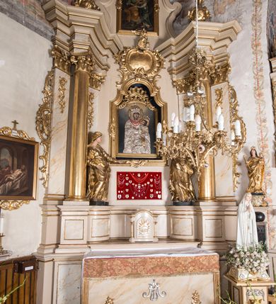 Zdjęcie nr 2: Nastawa ołtarzowa architektoniczna, jednoosiowa, jednokondygnacyjna ze zwieńczeniem, ustawiona na dwustrefowym cokole z wyodrębnionymi prostopadłościanami. Ołtarz kamienny, prostopadłościenny, w drewnianej obudowie. Mensa kamienna z marmurowym portatylem. Antepedium drewniane, w kształcie leżącego prostokąta, ujęte profilowaną ramą, z płaskorzeźbionym monogramem maryjnym oraz fragmentami ornamentu roślinnego. Tabernakulum w kształcie prostopadłościennej skrzynki o wypukłym licu, flankowanej parą kolumienek na cokołach, ustawionych pod kątem, dźwigających woluty oraz gzyms przyjmujący formę łuku segmentowego nadwieszonego. Drzwiczki w kształcie stojącego prostokąta zamkniętego łukiem półkolistym, w opasce, z płaskorzeźbionym przedstawieniem baranka apokaliptycznego, leżącego na księdze, w glorii. Nastawa ujęta dwiema parami pilastrów dekorowanych rocaille&#039;em i stojącą pomiędzy nimi parą kolumn o kapitelach kompozytowych dźwigających pełne belkowanie, wyłamane na ich osi, przerwane pośrodku. Na belkowaniu ustawione dwa wazony. W polu centralnym głęboka wnęka w formie stojącego prostokąta zamkniętego łukiem półkolistym nadwieszonym z uskokiem, ujęta profilowaną ramą, z obrazem Matki Boskiej z Dzieciątkiem w osobnej profilowanej ramie o kształcie stojącego prostokąta zamkniętego ornamentalnym łukiem. Ponad nią, w partii belkowania rokokowy kartusz z rytym monogramem Marii, a poniżej prostokątna płycina z wotami. Pole flankowane dwiema figurami kobiet stojącymi na ćwierćkolistych cokołach. Nastawa ujęta uszami utworzonymi z rocaille&#039;u. Zwieńczenie w formie stojącego prostokąta o wklęsłych bokach, ze spływami z uszakami po bokach, zamknięte gzymsem przyjmującym formę łuku segmentowego nadwieszonego z uskokiem, wyłamanego przy brzegach, dekorowanego rocaille&#039;em. W polu obraz „Nauczanie Marii przez Joachima” ujęty profilowaną ramą w kształcie stojącego prostokąta zamkniętego łukiem segmentowym nadwieszonym z uskokiem. 
Struktura marmoryzowana w kolorze beżowym; ornamentyka, profile i kolumny złocone.