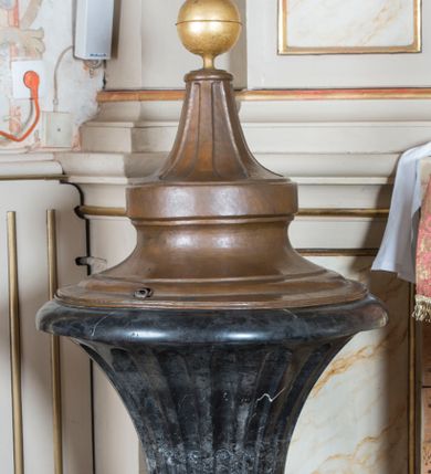 Zdjęcie nr 1: Chrzcielnica posadowiona na szerokiej podstawie na rzucie koła, z trzonem w dolnej części lekko wklęsłym zakończonym puklowanym pierścieniem, z czarą o formie rozchylonego kielicha z regularnymi wgłębieniami zakończonego gładkim, zaoblonym brzegiem. Pokrywa miedziana w formie odwróconego kielicha zakończonego pozłacanymi kulą z krzyżem. 