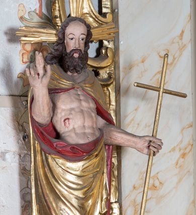 Zdjęcie nr 1: Figura ustawiona na żłobionym cokole na planie kwadratu, o wklęsłych bokach, zwężających się ku górze, dekorowanym perełkowaniem i liśćmi. Chrystus ukazany frontalnie, w wykroku, z głową delikatnie skierowaną w prawo. W lewej, wyciągniętej w bok ręce trzyma laskę zakończoną krzyżem, na której niegdyś zapewne wisiała chorągiew paschalna, prawą unosi w geście błogosławieństwa. Jezus ma pociągłą twarz o wysokim czole, półprzymknięte oczy, długi, prosty nos oraz małe, pełne usta. Twarz okolona jest silnie kręconą, rozdwajającą się brodą oraz kręconymi włosami sięgającymi ramion. Ciało ma szczupłe, silnie umięśnione. Chrystus ubrany jest w złocony płaszcz z czerwoną podszewką zapięty na piersi, zarzucony na ramiona i zawinięty z przodu postaci. Polichromia ciała naturalistyczna, z zaznaczonymi śladami męki. 