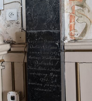 Zdjęcie nr 2: Na wysokim cokole oraz na niskiej marmurowej podstawie ustawiony jest filar z czarnego marmuru ujęty na dwóch końcach alabastrowym profilem, zakończony marmurową kulą. W partii cokołu wprawiona marmurowa płyta w formie leżącego prostokąta z inskrypcją „Oycze wieczny bez skończenia, / Jezu źródło zbawienne, /  Duchu dawco pocieszenia, Porusz serca kamienne, / Niechay godnie czołem biią, / W Troycy Bogu iedynemu, / Że dać raczył nam Maryą, / Ku zbawieniu naszemu.” Na trzonie filara inskrypcja „Jerżemu Ogończyk / Dubieckiemu / zmarłemu 1767. / Mateusz Władysław / Dubiecki / Kan(onik) Łucki i Krak(owski) / wdzięczny Syn / 1795. / wieczną pamiątkę / odnawia”. Ponad nią ryty kartusz z pustym polem. 