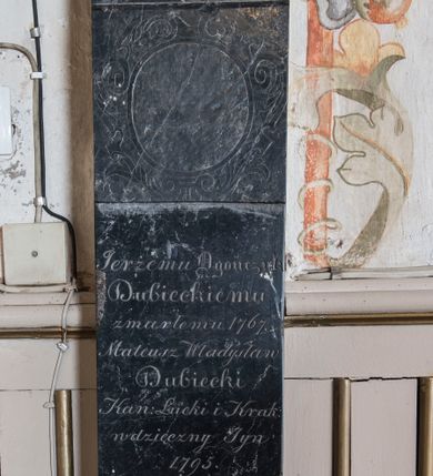 Zdjęcie nr 1: Na wysokim cokole oraz na niskiej marmurowej podstawie ustawiony jest filar z czarnego marmuru ujęty na dwóch końcach alabastrowym profilem, zakończony marmurową kulą. W partii cokołu wprawiona marmurowa płyta w formie leżącego prostokąta z inskrypcją „Oycze wieczny bez skończenia, / Jezu źródło zbawienne, /  Duchu dawco pocieszenia, Porusz serca kamienne, / Niechay godnie czołem biią, / W Troycy Bogu iedynemu, / Że dać raczył nam Maryą, / Ku zbawieniu naszemu.” Na trzonie filara inskrypcja „Jerżemu Ogończyk / Dubieckiemu / zmarłemu 1767. / Mateusz Władysław / Dubiecki / Kan(onik) Łucki i Krak(owski) / wdzięczny Syn / 1795. / wieczną pamiątkę / odnawia”. Ponad nią ryty kartusz z pustym polem. 