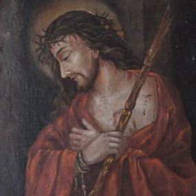 Zdjęcie nr 1: Obraz w formie stojącego prostokąta o ściętych narożach z przedstawieniem Chrystusa w półpostaci. Jezus zwrócony jest w trzech czwartych w prawo, z pochyloną głową, skrzyżowanymi rękami złożonymi na piersi, o związanych sznurem przegubach, w prawej dłoni trzyma trzcinę. Twarz ma szczupłą, o półprzymkniętych, migdałowatych oczach, lekko garbatym nosie i rozchylonych ustach, okoloną długimi, falowanymi, brązowymi włosami opadającymi na ramiona. Na głowie ma koronę cierniową, spod której spływają strużki krwi, wokół niej nimb. Chrystus na ramiona ma narzucony czerwony płaszcz, odsłaniający fragment poranionego torsu. Postać ukazana na ciemnobrązowym tle. 