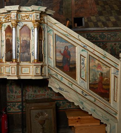 Zdjęcie nr 1: Ambona nadwieszona, przyścienna, wsparta na żelaznym pręcie. Kosz na planie ośmioboku; na ściankach płyciny w kształcie wąskich, stojących prostokątów, zamknięte trójbocznie z namalowanymi przedstawieniami symboli ewangelistów z podpisami: „S(ANCTUS) IOANNES”, „S(ANCTUS) MARCUS”, „S(ANCTUS) LVCAS”, „S(ANCTUS) MATHE[US]”. Ścianki wydzielone kolumnami na cokole o gładkich trzonach ze stylizowanymi kompozytowymi kapitelami, dźwigającymi pełne belkowanie wyłamane na ich osi. Na belkowaniu ornamenty małżowinowe. Parapet w formie silnie wystającego, profilowanego gzymsu. Z prawej strony dostawione, jednobiegowe schody z barierką zwieńczoną profilowanym gzymsem. Bariera z dwoma romboidalnymi płycinami, z przedstawieniami modlącego się świętego z modelem kościoła w dłoniach przed Marią i Chrystusem na obłokach oraz Chrystusa błogosławiącego z inskrypcją: „QUINIMO BEATI QVI AVDIVNT VERBVM DEI”. Baldachim na planie ośmioboku o profilowanym gzymsie wsparty na profilowanych listwach. Ambona marmoryzowana w tonacjach bieli, zieleni, błękit; detale złocone i srebrzone.