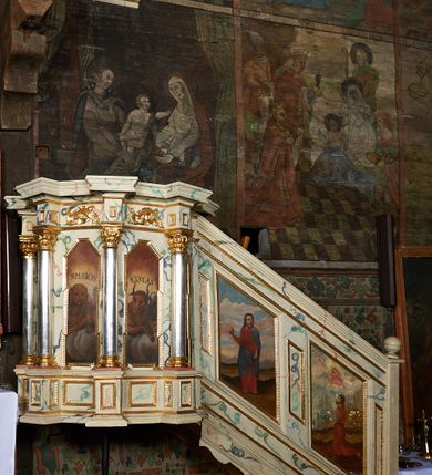 Zdjęcie nr 9: Ambona nadwieszona, przyścienna, wsparta na żelaznym pręcie. Kosz na planie ośmioboku; na ściankach płyciny w kształcie wąskich, stojących prostokątów, zamknięte trójbocznie z namalowanymi przedstawieniami symboli ewangelistów z podpisami: „S(ANCTUS) IOANNES”, „S(ANCTUS) MARCUS”, „S(ANCTUS) LVCAS”, „S(ANCTUS) MATHE[US]”. Ścianki wydzielone kolumnami na cokole o gładkich trzonach ze stylizowanymi kompozytowymi kapitelami, dźwigającymi pełne belkowanie wyłamane na ich osi. Na belkowaniu ornamenty małżowinowe. Parapet w formie silnie wystającego, profilowanego gzymsu. Z prawej strony dostawione, jednobiegowe schody z barierką zwieńczoną profilowanym gzymsem. Bariera z dwoma romboidalnymi płycinami, z przedstawieniami modlącego się świętego z modelem kościoła w dłoniach przed Marią i Chrystusem na obłokach oraz Chrystusa błogosławiącego z inskrypcją: „QUINIMO BEATI QVI AVDIVNT VERBVM DEI”. Baldachim na planie ośmioboku o profilowanym gzymsie wsparty na profilowanych listwach. Ambona marmoryzowana w tonacjach bieli, zieleni, błękit; detale złocone i srebrzone.