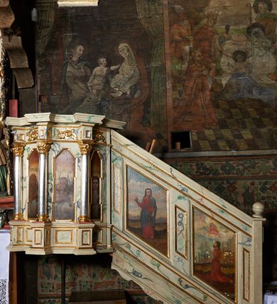 Zdjęcie nr 2: Ambona nadwieszona, przyścienna, wsparta na żelaznym pręcie. Kosz na planie ośmioboku; na ściankach płyciny w kształcie wąskich, stojących prostokątów, zamknięte trójbocznie z namalowanymi przedstawieniami symboli ewangelistów z podpisami: „S(ANCTUS) IOANNES”, „S(ANCTUS) MARCUS”, „S(ANCTUS) LVCAS”, „S(ANCTUS) MATHE[US]”. Ścianki wydzielone kolumnami na cokole o gładkich trzonach ze stylizowanymi kompozytowymi kapitelami, dźwigającymi pełne belkowanie wyłamane na ich osi. Na belkowaniu ornamenty małżowinowe. Parapet w formie silnie wystającego, profilowanego gzymsu. Z prawej strony dostawione, jednobiegowe schody z barierką zwieńczoną profilowanym gzymsem. Bariera z dwoma romboidalnymi płycinami, z przedstawieniami modlącego się świętego z modelem kościoła w dłoniach przed Marią i Chrystusem na obłokach oraz Chrystusa błogosławiącego z inskrypcją: „QUINIMO BEATI QVI AVDIVNT VERBVM DEI”. Baldachim na planie ośmioboku o profilowanym gzymsie wsparty na profilowanych listwach. Ambona marmoryzowana w tonacjach bieli, zieleni, błękit; detale złocone i srebrzone.
