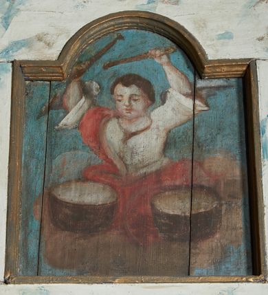 Zdjęcie nr 3: Balustrada chóru muzycznego dziewięcioosiowa, jednokondygnacyjna, od spodu z podwieszonym lambrekinem, na osi środkowej wypukła. Osie flankowane kolumienkami ustawionymi na cokołach, które podtrzymują imposty ustawione pod kątem, wyłamujące profilowany gzyms balustrady. Trzony kolumienek malowane na czarno, kapitele stylizowane na korynckie, złocone. W każdej osi umieszczona płycina w kształcie stojącego prostokąta zamknięta łukiem nadwieszonym. Kolejno od lewej strony malowane w płycinach obrazy: aniołek grający na trąbce, aniołek grający na bębnach, ponownie aniołek grający na trąbce i aniołek grający na skrzypach. Na środku osi płycina w kształcie stojącego prostokąta zamknięta trójkątnie o wyłamanym zwieńczeniu, w polu przedstawienie króla Dawida grającego na harfie. U góry banderola z napisem „LAUDATE DOMINUM IN CITHARA”. Po drugiej stronie balustrady, kolejno od lewej: aniołek grający na wiolonczeli, aniołek grający na trąbce, aniołek grający na flecie i aniołek grający na mandolinie. Wszystkie postacie ukazane na jasnobłękitnym tle, na chmurze białych obłoków. Anioły półnagie, ubrane w czerwone szaty. Struktura balustrady marmoryzowana na biało z niebieskimi przetarciami, detale złocone i malowane na czarno.
