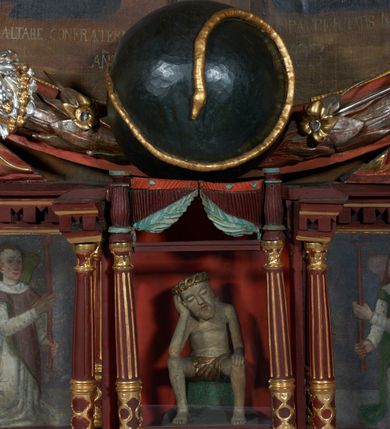 Zdjęcie nr 2: Figura pełnoplastyczna przedstawiająca Chrystusa Frasobliwego. Chrystus ukazany w pozycji siedzącej na kamiennym postumencie, wspierający prawą ręką głowę, a lewą rękę opierający na prawym kolanie, z głową delikatnie przechyloną na prawą stronę. Ciało o szczupłej sylwetce. Twarz podłużna, z długim i szerokim nosem, przymkniętymi oczami, okolona krótką i jasną brodą. Włosy jasne, średniej długości opadające na plecy. Na głowie Chrystus ma założoną koronę cierniową złożoną z przeplatających się symetrycznie dwóch gałązek. Perizonium złocone, ciasno oplatające biodra, silnie drapowane. Polichromia w odsłoniętych partiach ciała naturalistyczna. Cokół pomalowany na kolor zielony.