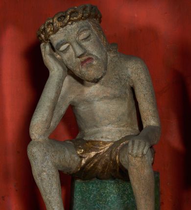 Zdjęcie nr 1: Figura pełnoplastyczna przedstawiająca Chrystusa Frasobliwego. Chrystus ukazany w pozycji siedzącej na kamiennym postumencie, wspierający prawą ręką głowę, a lewą rękę opierający na prawym kolanie, z głową delikatnie przechyloną na prawą stronę. Ciało o szczupłej sylwetce. Twarz podłużna, z długim i szerokim nosem, przymkniętymi oczami, okolona krótką i jasną brodą. Włosy jasne, średniej długości opadające na plecy. Na głowie Chrystus ma założoną koronę cierniową złożoną z przeplatających się symetrycznie dwóch gałązek. Perizonium złocone, ciasno oplatające biodra, silnie drapowane. Polichromia w odsłoniętych partiach ciała naturalistyczna. Cokół pomalowany na kolor zielony.