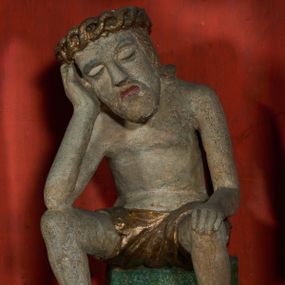 Zdjęcie nr 1: Figura pełnoplastyczna przedstawiająca Chrystusa Frasobliwego. Chrystus ukazany w pozycji siedzącej na kamiennym postumencie, wspierający prawą ręką głowę, a lewą rękę opierający na prawym kolanie, z głową delikatnie przechyloną na prawą stronę. Ciało o szczupłej sylwetce. Twarz podłużna, z długim i szerokim nosem, przymkniętymi oczami, okolona krótką i jasną brodą. Włosy jasne, średniej długości opadające na plecy. Na głowie Chrystus ma założoną koronę cierniową złożoną z przeplatających się symetrycznie dwóch gałązek. Perizonium złocone, ciasno oplatające biodra, silnie drapowane. Polichromia w odsłoniętych partiach ciała naturalistyczna. Cokół pomalowany na kolor zielony.