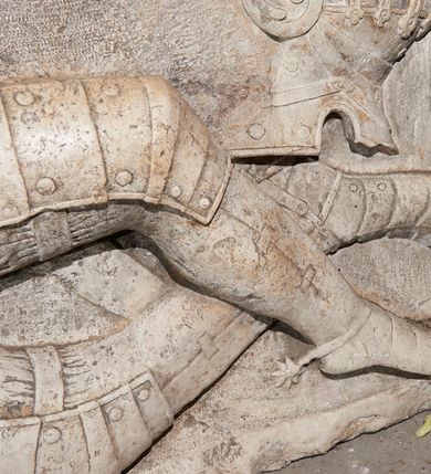 Zdjęcie nr 3: Płyta nagrobna z płaskorzeźbionym przedstawieniem rycerza w typie sansovinowskim, ukazanym w półśnie. Rycerz ułożony na prawym boku, prawą ręką podpierający głowę spoczywającą na poduszce, z lewą złożoną na pancerzu; nogi zgięte w kolanach i skrzyżowane. W prawym górnym narożu płyty umieszczony hełm z opuszczoną zasłoną prętową i pióropuszem. Rycerz ubrany w zbroję turniejową, z przypiętą do pasa po prawej stronie szablą, batorówką i ostrogami na butach. Włosy ułożone w stylu polskim, ma wąsy. Wzdłuż krawędzi prawego boku na kamieniu płyty nagrobnej znajduje się inskrypcja. Bezpośrednio ponad głową zmarłego napis „VIVIENDO MOBIMVR”, zaś nad hełmem „MORIENDO VIVIMVS”. Nad płytą nagrobną barokowy kartusz z tarczą herbową. Tarcza owalna, wypukła, czteropolowa, ujęta ornamentem rollwerkowym. W skwadrowanym polu tarczy umieszczono zatarte godła herbów: Rawicz (pole I), Topór (pole II), Rogala (pole III), Półkozic (pole IV).
