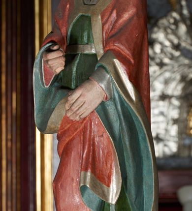 Zdjęcie nr 4: Łuk tęczowy o półkolistym wykroju wsparty na kroksztynach. Belka profilowana, współczesna (z czasów ostatniej konserwacji, nawiązująca do poprzedniej gotyckiej). W centrum krucyfiks z postacią Chrystusa umarłego, po prawej św. Jan Ewangelista, po lewej Matka Boska i św. Maria Magdalena. Chrystus przybity do krzyża trzema gwoździami, sylwetka w delikatnym zwisie, z głową przechyloną na prawe ramię, o silnie podkreślonej anatomii ciała, z zaznaczonymi śladami męki. Perizonium w formie tkaniny przewiązanej na prawym biodrze. Twarz podłużna, okolona zarostem; włosy długie spływające na prawe ramię w kręcone pukle, na głowie korona cierniowa. Po prawej stronie rzeźba św. Jana Ewangelisty, ukazanego w postawie stojącej, zwróconego w trzech czwartych w prawo, lewą ręką przytrzymującego z przodu płaszcz. Święty jest ubrany w długą, zieloną suknię z długimi rękawami oraz czerwony płaszcz, spięty na piersi, zdobiony na brzegach grubą lamelką. Twarz owalna, policzki silnie zarumienione, małe usta, długi i wąski nos, wzrok skierowany przed siebie, zmarszczone brwi. Włosy jasne, spływające do ramion ciasno ułożonymi puklami. Po lewej stronie krucyfiksu rzeźba św. Marii Magdaleny ukazana w pozycji klęczącej, z prawego profilu, z wyciągniętymi w stronę krzyża dłońmi. Święta jest ubrana w długą, czerwoną suknię oraz obszerny zielony płaszcz ze srebrną podszewką, na głowie ma biały welon. Twarz owalna, z wyraźnie zaznaczonym podbródkiem, zmarszczone brwi; spod welonu spływają na lewe ramię długie i jasne włosy. Za nią rzeźba Matki Boskiej ustawiona w kontrapoście, z prawą nogą ugiętą w kolanie, ze skrzyżowanymi na piersi rękami. Maria jest ubrana w długą, bordową suknię oraz błękitny płaszcz z czerwoną podszewką. Twarz szeroka, z wyraźnie zaznaczonym podbródkiem, wzrok skierowany w dal, zmarszczone brwi. Rzeźby ustawione na półkolistych, zielonych cokolikach. Polichromia w odsłoniętych partiach ciała naturalistyczna, detale złocone. 
