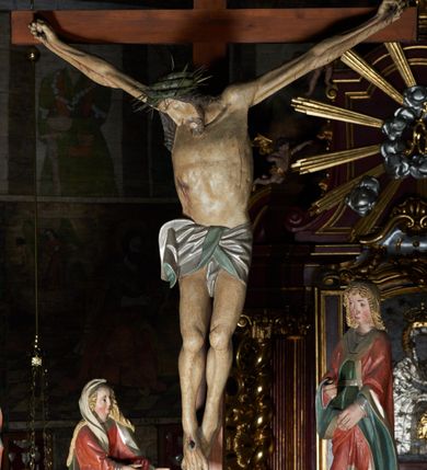 Zdjęcie nr 1: Krucyfiks w typie Cristo morte. Chrystus przybity do krzyża trzema gwoździami, sylwetka w delikatnym zwisie, z głową przechyloną na prawe ramię, o silnie podkreślonej anatomii ciała, z zaznaczonymi śladami męki. Perizonium w formie tkaniny przewiązanej na prawym biodrze. Twarz podłużna, okolona zarostem; włosy długie spływające na prawe ramię w kręcone pukle, na głowie korona cierniowa. Polichromia w odsłoniętych partiach ciała naturalistyczna.