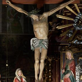 Zdjęcie nr 1: Krucyfiks w typie Cristo morte. Chrystus przybity do krzyża trzema gwoździami, sylwetka w delikatnym zwisie, z głową przechyloną na prawe ramię, o silnie podkreślonej anatomii ciała, z zaznaczonymi śladami męki. Perizonium w formie tkaniny przewiązanej na prawym biodrze. Twarz podłużna, okolona zarostem; włosy długie spływające na prawe ramię w kręcone pukle, na głowie korona cierniowa. Polichromia w odsłoniętych partiach ciała naturalistyczna.