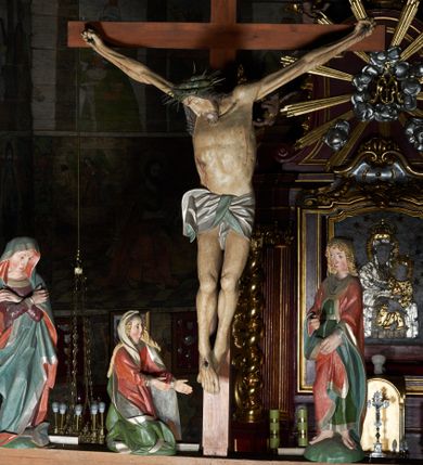 Zdjęcie nr 5: Krucyfiks w typie Cristo morte. Chrystus przybity do krzyża trzema gwoździami, sylwetka w delikatnym zwisie, z głową przechyloną na prawe ramię, o silnie podkreślonej anatomii ciała, z zaznaczonymi śladami męki. Perizonium w formie tkaniny przewiązanej na prawym biodrze. Twarz podłużna, okolona zarostem; włosy długie spływające na prawe ramię w kręcone pukle, na głowie korona cierniowa. Polichromia w odsłoniętych partiach ciała naturalistyczna.
