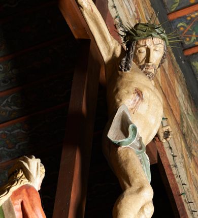 Zdjęcie nr 6: Krucyfiks w typie Cristo morte. Chrystus przybity do krzyża trzema gwoździami, sylwetka w delikatnym zwisie, z głową przechyloną na prawe ramię, o silnie podkreślonej anatomii ciała, z zaznaczonymi śladami męki. Perizonium w formie tkaniny przewiązanej na prawym biodrze. Twarz podłużna, okolona zarostem; włosy długie spływające na prawe ramię w kręcone pukle, na głowie korona cierniowa. Polichromia w odsłoniętych partiach ciała naturalistyczna.