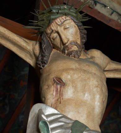 Zdjęcie nr 3: Krucyfiks w typie Cristo morte. Chrystus przybity do krzyża trzema gwoździami, sylwetka w delikatnym zwisie, z głową przechyloną na prawe ramię, o silnie podkreślonej anatomii ciała, z zaznaczonymi śladami męki. Perizonium w formie tkaniny przewiązanej na prawym biodrze. Twarz podłużna, okolona zarostem; włosy długie spływające na prawe ramię w kręcone pukle, na głowie korona cierniowa. Polichromia w odsłoniętych partiach ciała naturalistyczna.