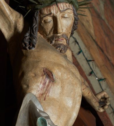 Zdjęcie nr 2: Krucyfiks w typie Cristo morte. Chrystus przybity do krzyża trzema gwoździami, sylwetka w delikatnym zwisie, z głową przechyloną na prawe ramię, o silnie podkreślonej anatomii ciała, z zaznaczonymi śladami męki. Perizonium w formie tkaniny przewiązanej na prawym biodrze. Twarz podłużna, okolona zarostem; włosy długie spływające na prawe ramię w kręcone pukle, na głowie korona cierniowa. Polichromia w odsłoniętych partiach ciała naturalistyczna.