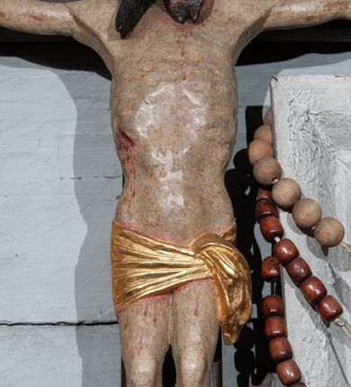 Zdjęcie nr 3: Krzyż prosty, współczesny. Rzeźba zawieszona na krzyżu na wyprostowanych ramionach, figura w typie Christo vivo, głowa delikatnie przechylona na prawe ramię; nogi ugięte w kolanach, stopy przebite jednym gwoździem w układzie prawa na lewą. Twarz Chrystusa pociągła, o wyraźnych rysach, dużym i wąskim nosie; okolona krótkim zarostem; na głowie szeroka korona cierniowa. Sylwetka wychudzona, z wydatną klatką piersiową i wąską talią. Perizonium przewiązane na lewym boku, ciasno oplatające biodra. Nad głowią Chrystusa znajduje się titulus w formie białej banderoli z napisem „INRI”. Polichromia naturalistyczna w odsłoniętych partiach ciała z zaznaczonymi śladami męki, perizonium złocone.