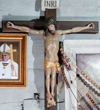 Zdjęcie nr 1: Krzyż prosty, współczesny. Rzeźba zawieszona na krzyżu na wyprostowanych ramionach, figura w typie Christo vivo, głowa delikatnie przechylona na prawe ramię; nogi ugięte w kolanach, stopy przebite jednym gwoździem w układzie prawa na lewą. Twarz Chrystusa pociągła, o wyraźnych rysach, dużym i wąskim nosie; okolona krótkim zarostem; na głowie szeroka korona cierniowa. Sylwetka wychudzona, z wydatną klatką piersiową i wąską talią. Perizonium przewiązane na lewym boku, ciasno oplatające biodra. Nad głowią Chrystusa znajduje się titulus w formie białej banderoli z napisem „INRI”. Polichromia naturalistyczna w odsłoniętych partiach ciała z zaznaczonymi śladami męki, perizonium złocone.