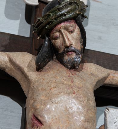 Zdjęcie nr 4: Krzyż prosty, współczesny. Rzeźba zawieszona na krzyżu na wyprostowanych ramionach, figura w typie Christo vivo, głowa delikatnie przechylona na prawe ramię; nogi ugięte w kolanach, stopy przebite jednym gwoździem w układzie prawa na lewą. Twarz Chrystusa pociągła, o wyraźnych rysach, dużym i wąskim nosie; okolona krótkim zarostem; na głowie szeroka korona cierniowa. Sylwetka wychudzona, z wydatną klatką piersiową i wąską talią. Perizonium przewiązane na lewym boku, ciasno oplatające biodra. Nad głowią Chrystusa znajduje się titulus w formie białej banderoli z napisem „INRI”. Polichromia naturalistyczna w odsłoniętych partiach ciała z zaznaczonymi śladami męki, perizonium złocone.