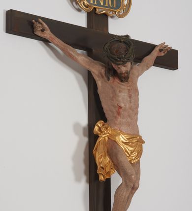 Zdjęcie nr 2: Krucyfiks z rzeźbą Chrystusa w typie Cristo morte. Rzeźba pełna; ciało w dużym zwisie, o esowato wygiętej sylwetce; głowa przechylona na prawe ramię; nogi ugięte w kolanach, stopy przebite jednym gwoździem w układzie prawa na lewą. Twarz pociągła, o wyraźnych rysach, okolona krótkim zarostem. Na głowie szeroka korona cierniowa. Sylwetka Chrystusa wychudzona, ciało z zaznaczonymi żebrami klatki piersiowej i mostkiem. Perizonium przewiązane na prawym boku. Nad głową Chrystusa znajduje się owalny kartusz obwiedziony ażurowym ornamentem małżowinowo-chrząstkowym z napisem „INRI” w polu. Polichromia naturalistyczna w odsłoniętych partiach ciała z zaznaczonymi śladami męki, perizonium złocone.