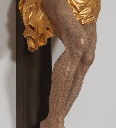 Zdjęcie nr 3: Krucyfiks z rzeźbą Chrystusa w typie Cristo morte. Rzeźba pełna; ciało w dużym zwisie, o esowato wygiętej sylwetce; głowa przechylona na prawe ramię; nogi ugięte w kolanach, stopy przebite jednym gwoździem w układzie prawa na lewą. Twarz pociągła, o wyraźnych rysach, okolona krótkim zarostem. Na głowie szeroka korona cierniowa. Sylwetka Chrystusa wychudzona, ciało z zaznaczonymi żebrami klatki piersiowej i mostkiem. Perizonium przewiązane na prawym boku. Nad głową Chrystusa znajduje się owalny kartusz obwiedziony ażurowym ornamentem małżowinowo-chrząstkowym z napisem „INRI” w polu. Polichromia naturalistyczna w odsłoniętych partiach ciała z zaznaczonymi śladami męki, perizonium złocone.