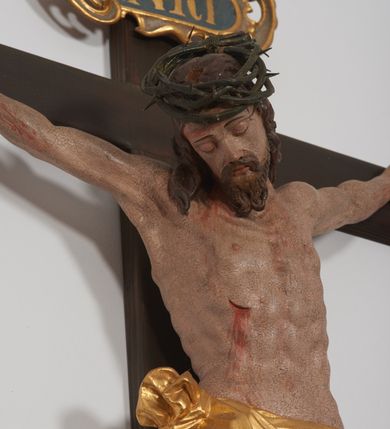 Zdjęcie nr 4: Krucyfiks z rzeźbą Chrystusa w typie Cristo morte. Rzeźba pełna; ciało w dużym zwisie, o esowato wygiętej sylwetce; głowa przechylona na prawe ramię; nogi ugięte w kolanach, stopy przebite jednym gwoździem w układzie prawa na lewą. Twarz pociągła, o wyraźnych rysach, okolona krótkim zarostem. Na głowie szeroka korona cierniowa. Sylwetka Chrystusa wychudzona, ciało z zaznaczonymi żebrami klatki piersiowej i mostkiem. Perizonium przewiązane na prawym boku. Nad głową Chrystusa znajduje się owalny kartusz obwiedziony ażurowym ornamentem małżowinowo-chrząstkowym z napisem „INRI” w polu. Polichromia naturalistyczna w odsłoniętych partiach ciała z zaznaczonymi śladami męki, perizonium złocone.