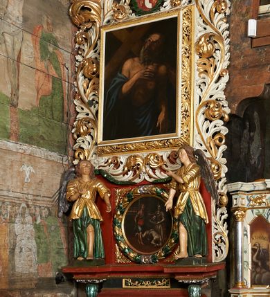 Zdjęcie nr 1: Ołtarz jednokondygnacyjny, jednoosiowy ze zwieńczeniem, ustawiony na mensie. Mensa drewniana, prostopadłościenna, z przodu malowana na czerwono płycina z krzyżem oraz dwiema skrzyżowanymi gałązkami palm w polu. Cokół nastawy flankowany przez dwie rzeźby aniołów; pośrodku obraz „Ścięcie św. Jana Chrzciciela” w owalu. Kondygnacja złożona z obrazu z przedstawieniem św. Andrzeja w kształcie stojącego prostokąta otoczonego przez bujne wici liści akantu. Nad obrazem herb Szreniawa z syglami w polu tarczy A(NDRZEJ) S(TRZAŁKOWSKI) P(ROBOSZCZ) R(ACŁAWICKI). Tarcza zwieńczona otwartą koroną, nad którą umieszczono skrzydlatą główkę aniołka skierowaną na wprost. W zwieńczeniu ołtarza owalny obraz „Święty Antoni Padewski” w ramie z bujnego akantu. U szczytu oraz po bokach zwieńczenia trzy rzeźby aniołów. Struktura polichromowana w kolorze jasnego beżu; detale, ornamentyka i profilowania złocone.
