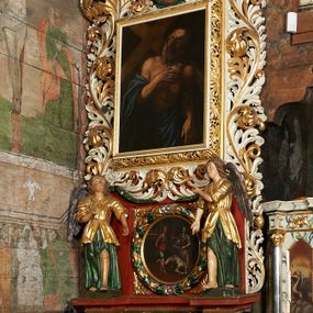 Zdjęcie nr 1: Ołtarz jednokondygnacyjny, jednoosiowy ze zwieńczeniem, ustawiony na mensie. Mensa drewniana, prostopadłościenna, z przodu malowana na czerwono płycina z krzyżem oraz dwiema skrzyżowanymi gałązkami palm w polu. Cokół nastawy flankowany przez dwie rzeźby aniołów; pośrodku obraz „Ścięcie św. Jana Chrzciciela” w owalu. Kondygnacja złożona z obrazu z przedstawieniem św. Andrzeja w kształcie stojącego prostokąta otoczonego przez bujne wici liści akantu. Nad obrazem herb Szreniawa z syglami w polu tarczy A(NDRZEJ) S(TRZAŁKOWSKI) P(ROBOSZCZ) R(ACŁAWICKI). Tarcza zwieńczona otwartą koroną, nad którą umieszczono skrzydlatą główkę aniołka skierowaną na wprost. W zwieńczeniu ołtarza owalny obraz „Święty Antoni Padewski” w ramie z bujnego akantu. U szczytu oraz po bokach zwieńczenia trzy rzeźby aniołów. Struktura polichromowana w kolorze jasnego beżu; detale, ornamentyka i profilowania złocone.
