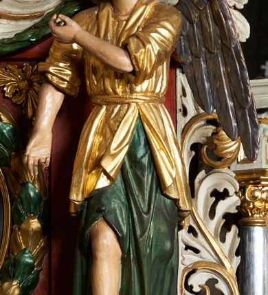 Zdjęcie nr 3: Rzeźby aniołów flankujące cokół nastawy ołtarzowej ukazane są w pozycji stojącej, zwrócone przeciwstawnie, w trzech czwartych ku środkowi nastawy z wyciągniętymi doń rękami. Ubrane w długie zielone suknie, z rozcięciem odsłaniającym jedną nogę powyżej kolana oraz złoconą tunikę z podwiniętymi rękawami do łokci i kołnierzykiem. Anioły mają po jednym skrzydle, usytuowanym od strony zewnętrznej. Modelunek postaci jest sztywny. Anioły osadzone po bokach zwieńczenia ukazane są w pozycji klęczącej, przeciwstawnie do siebie, zwrócone w trzech czwartych ku środkowi, z wyciągniętymi doń rękami. Ubrane w długie jasnozielone suknie oraz złocone tuniki z podwiniętymi rękawami do łokci i kołnierzykiem. Anioły mają dwa skrzydła, szeroko rozłożone. Anioł u szczytu nastawy jest ukazany w pozycji stojącej, frontalnie, w delikatnym kontrapoście, z rozłożonymi na boki rękami, z głową zwróconą w prawo. Ubrany analogicznie jak anioły flankujące zwieńczenie. 
Twarze wszystkich aniołów owalne, z silnie wysuniętym podbródkiem, zarumienionymi policzkami i małymi oczami. Włosy długie, ciemnobrązowe, kędzierzawe, z przedziałkiem pośrodku, opadające na plecy. Polichromia w odsłoniętych partiach ciała naturalistyczna, skrzydła srebrzone. 
