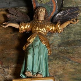 Zdjęcie nr 1: Rzeźby aniołów flankujące cokół nastawy ołtarzowej ukazane są w pozycji stojącej, zwrócone przeciwstawnie, w trzech czwartych ku środkowi nastawy z wyciągniętymi doń rękami. Ubrane w długie zielone suknie, z rozcięciem odsłaniającym jedną nogę powyżej kolana oraz złoconą tunikę z podwiniętymi rękawami do łokci i kołnierzykiem. Anioły mają po jednym skrzydle, usytuowanym od strony zewnętrznej. Modelunek postaci jest sztywny. Anioły osadzone po bokach zwieńczenia ukazane są w pozycji klęczącej, przeciwstawnie do siebie, zwrócone w trzech czwartych ku środkowi, z wyciągniętymi doń rękami. Ubrane w długie jasnozielone suknie oraz złocone tuniki z podwiniętymi rękawami do łokci i kołnierzykiem. Anioły mają dwa skrzydła, szeroko rozłożone. Anioł u szczytu nastawy jest ukazany w pozycji stojącej, frontalnie, w delikatnym kontrapoście, z rozłożonymi na boki rękami, z głową zwróconą w prawo. Ubrany analogicznie jak anioły flankujące zwieńczenie. 
Twarze wszystkich aniołów owalne, z silnie wysuniętym podbródkiem, zarumienionymi policzkami i małymi oczami. Włosy długie, ciemnobrązowe, kędzierzawe, z przedziałkiem pośrodku, opadające na plecy. Polichromia w odsłoniętych partiach ciała naturalistyczna, skrzydła srebrzone. 

