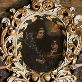 Zdjęcie nr 1: Obraz w kształcie owalu z przedstawieniem św. Antoniego Padewskiego. Święty ukazany w centrum kompozycji, w półpostaci, zwrócony w trzech czwartych w lewo, z Dzieciątkiem Jezus trzymanym na księdze w lewej ręce oraz gałązką lilii w drugiej. Ubrany w habit franciszkański, z tonsurą na głowie. Twarz owalna, z silnie zarumienionymi policzkami, oczy przymknięte, wzrok wpatrzony w dół, odstające uszy. Dzieciątko ukazane w pozycji siedzącej, zwrócone w trzech czwartych w prawo, prawą ręką czyniące gest błogosławieństwa. Ubrane jest w długą, przezroczystą sukienkę. W górnej części obrazu, po prawej stronie snop światła wyłaniający się z obłoków. Tło jednolite, ciemne. Kolorystyka obrazu ciemna. 

