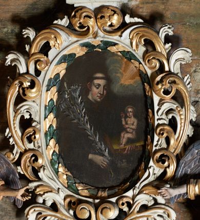 Zdjęcie nr 2: Obraz w kształcie owalu z przedstawieniem św. Antoniego Padewskiego. Święty ukazany w centrum kompozycji, w półpostaci, zwrócony w trzech czwartych w lewo, z Dzieciątkiem Jezus trzymanym na księdze w lewej ręce oraz gałązką lilii w drugiej. Ubrany w habit franciszkański, z tonsurą na głowie. Twarz owalna, z silnie zarumienionymi policzkami, oczy przymknięte, wzrok wpatrzony w dół, odstające uszy. Dzieciątko ukazane w pozycji siedzącej, zwrócone w trzech czwartych w prawo, prawą ręką czyniące gest błogosławieństwa. Ubrane jest w długą, przezroczystą sukienkę. W górnej części obrazu, po prawej stronie snop światła wyłaniający się z obłoków. Tło jednolite, ciemne. Kolorystyka obrazu ciemna. 
