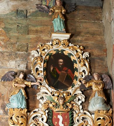 Zdjęcie nr 2: Rzeźby aniołów flankujące cokół nastawy ołtarzowej ukazane w pozycji stojącej, zwrócone przeciwstawnie, w trzech czwartych ku środkowi nastawy z wyciągniętymi doń rękami. Ubrane w długie zielone suknie, z rozcięciem odsłaniającym jedną nogę powyżej kolana oraz złoconą tunikę z podwiniętymi rękawami do łokci i kołnierzykiem. Anioły mają po jednym skrzydle, usytuowanym od strony zewnętrznej. Modelunek postaci jest sztywny. Anioły osadzone po bokach zwieńczenia ukazane są w pozycji klęczącej, przeciwstawnie do siebie, zwrócone w trzech czwartych ku środkowi, z wyciągniętymi doń rękami. Ubrane w długie jasnozielone suknie oraz złocone tuniki z podwiniętymi rękawami do łokci i kołnierzykiem. Anioły mają dwa skrzydła, szeroko rozłożone. Anioł u szczytu nastawy jest ukazany w pozycji stojącej, frontalnie, w delikatnym kontrapoście, z wyciągniętymi do przodu rękami, z głową zwróconą w prawo, z rozłożonymi szeroko skrzydłami. Ubrany analogicznie jak anioły flankujące zwieńczenie. 
Twarze wszystkich aniołów owalne, z silnie wysuniętym podbródkiem, zarumienionymi policzkami i małymi oczami. Włosy długie, ciemnobrązowe, kędzierzawe, z przedziałkiem pośrodku, opadające na plecy. Polichromia w odsłoniętych partiach ciała naturalistyczna, skrzydła srebrzone. 
