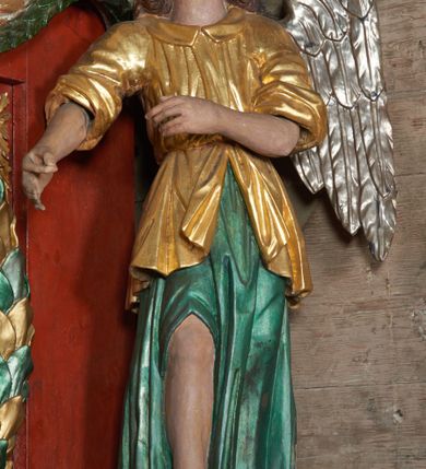 Zdjęcie nr 5: Rzeźby aniołów flankujące cokół nastawy ołtarzowej ukazane w pozycji stojącej, zwrócone przeciwstawnie, w trzech czwartych ku środkowi nastawy z wyciągniętymi doń rękami. Ubrane w długie zielone suknie, z rozcięciem odsłaniającym jedną nogę powyżej kolana oraz złoconą tunikę z podwiniętymi rękawami do łokci i kołnierzykiem. Anioły mają po jednym skrzydle, usytuowanym od strony zewnętrznej. Modelunek postaci jest sztywny. Anioły osadzone po bokach zwieńczenia ukazane są w pozycji klęczącej, przeciwstawnie do siebie, zwrócone w trzech czwartych ku środkowi, z wyciągniętymi doń rękami. Ubrane w długie jasnozielone suknie oraz złocone tuniki z podwiniętymi rękawami do łokci i kołnierzykiem. Anioły mają dwa skrzydła, szeroko rozłożone. Anioł u szczytu nastawy jest ukazany w pozycji stojącej, frontalnie, w delikatnym kontrapoście, z wyciągniętymi do przodu rękami, z głową zwróconą w prawo, z rozłożonymi szeroko skrzydłami. Ubrany analogicznie jak anioły flankujące zwieńczenie. 
Twarze wszystkich aniołów owalne, z silnie wysuniętym podbródkiem, zarumienionymi policzkami i małymi oczami. Włosy długie, ciemnobrązowe, kędzierzawe, z przedziałkiem pośrodku, opadające na plecy. Polichromia w odsłoniętych partiach ciała naturalistyczna, skrzydła srebrzone. 
